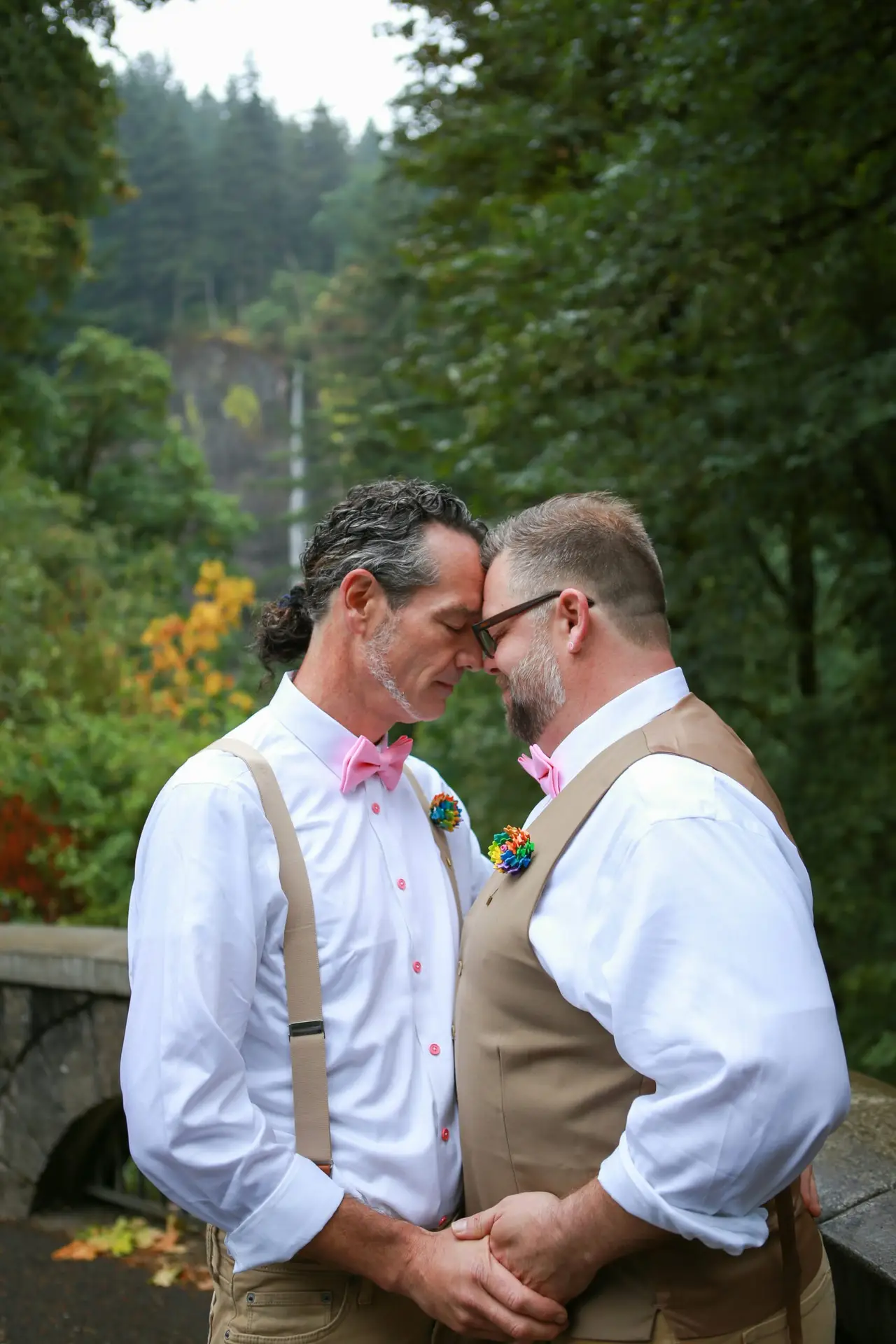 Couple gay se tenant tendrement l’un l’autre, front contre front, lors de leur mariage en plein air entouré de nature verdoyante